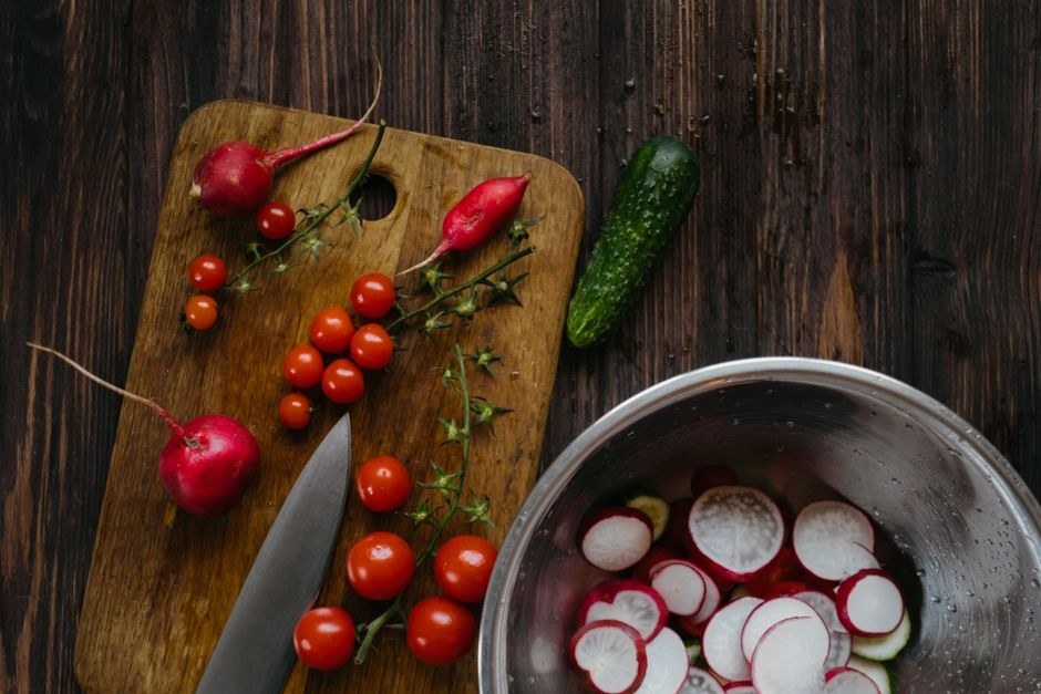 Fresh radishes, tomatoes, cucumber, herbs and a knife arranged for supper preparation.
